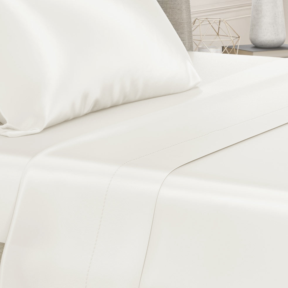 Close-up of a ivory silk sheet on a bed, highlighting its delicate stitching and sheen