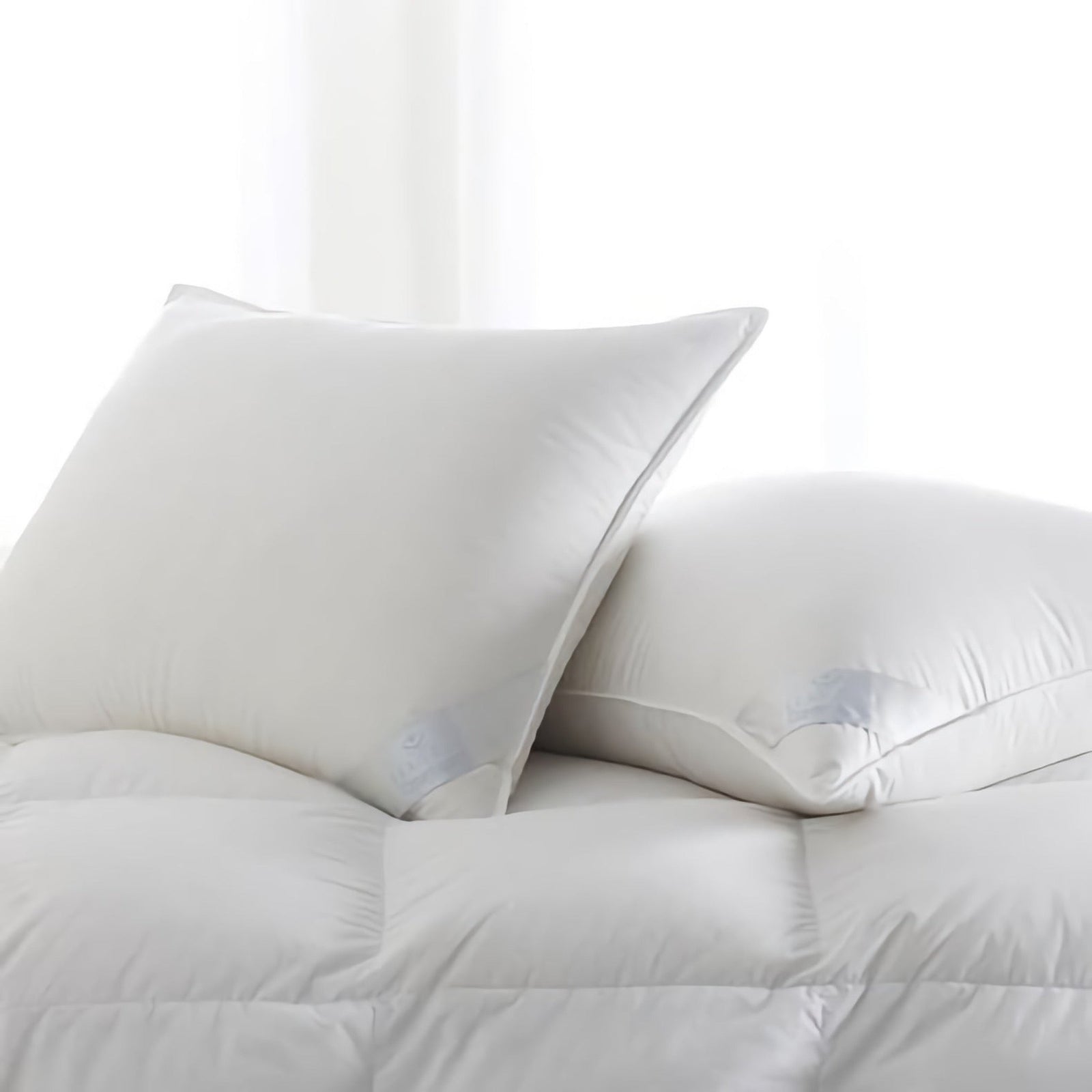 Two white pillows rest on a matching white, quilted comforter. The background is softly lit, creating a clean and minimal look.