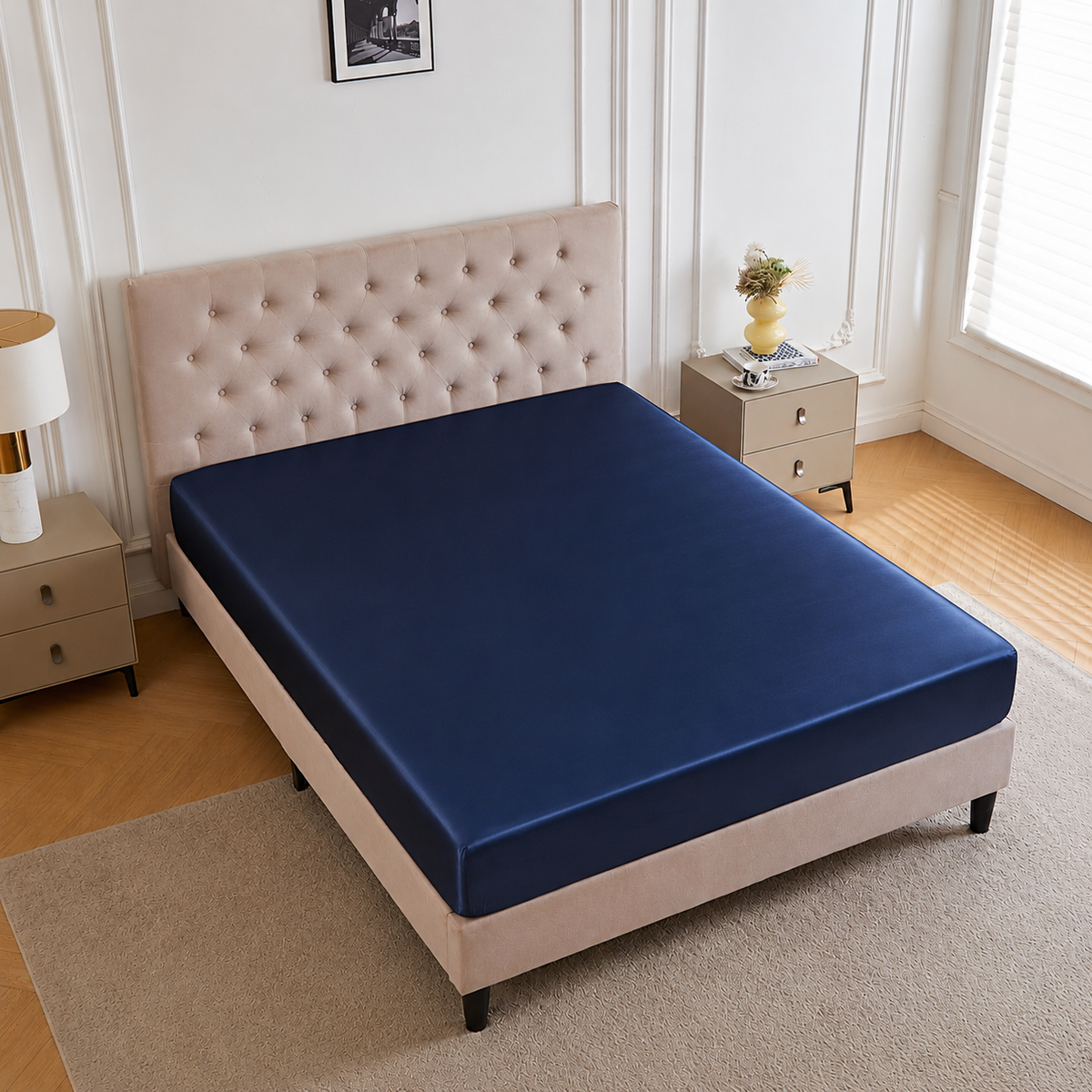 A neatly made bed with a 30 Momme Silk Fitted Sheet in navy, beige tufted headboard, and a vase on the nightstand.