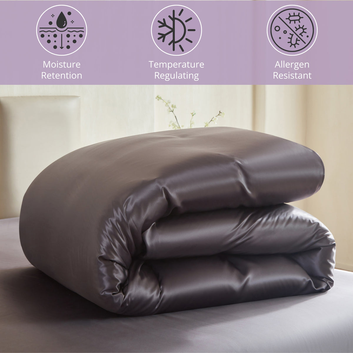 Folded dark gray silk comforter on a bed with moisture retention, temperature regulating, and allergen-resistant icons above.