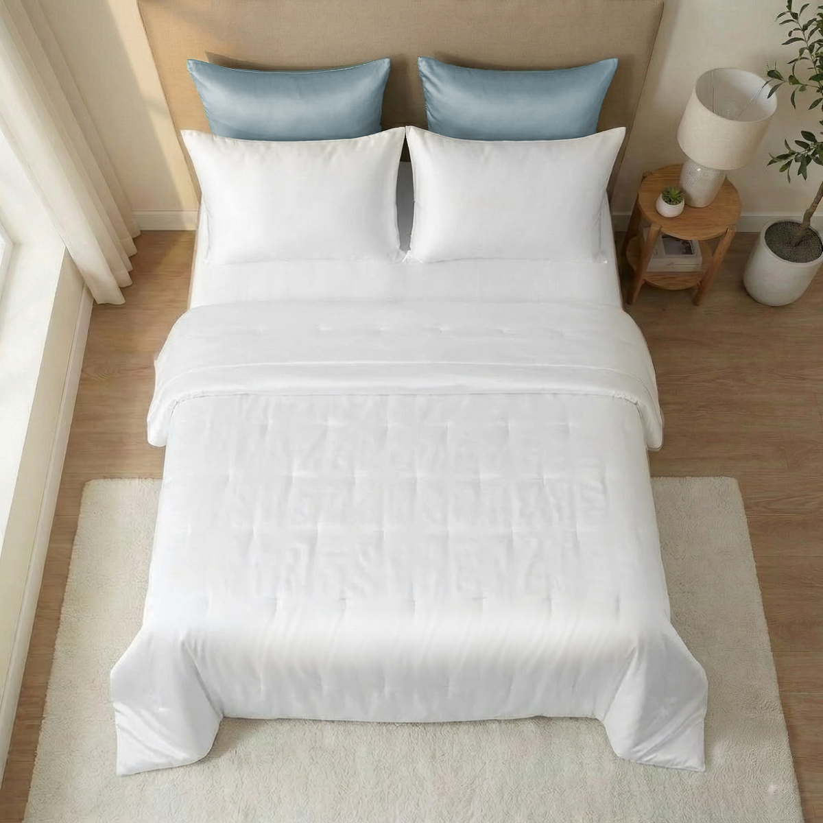 A neatly made bed with a white Mulberry silk bedspread, blue accent pillows, a nightstand, and a small potted plant.