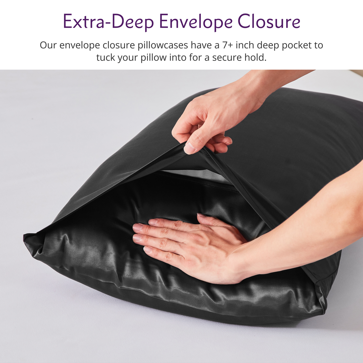 Hands placing a pillow into a black Mulberry silk pillowcase with a deep envelope closure on a white surface.