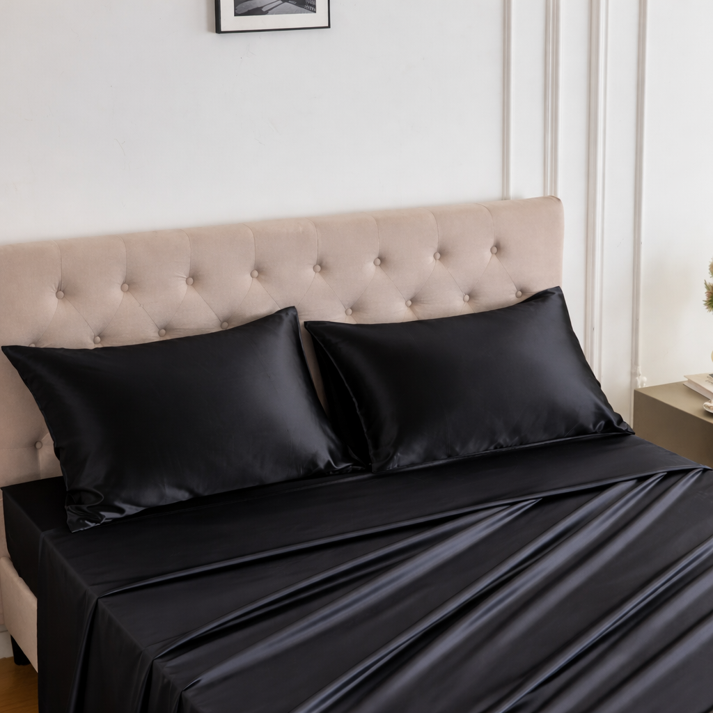 A beige tufted headboard with a bed made up in luxury silk sheet set and two black satin pillows.