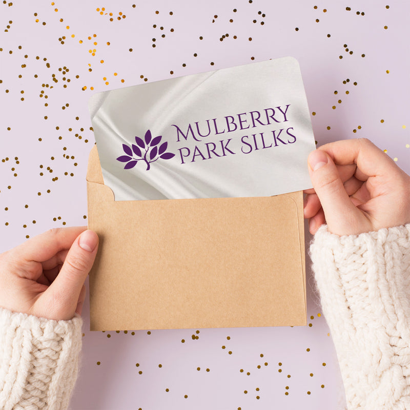 Person holding a Mulberry Park Silks branded gift card against a light purple background with gold dots.