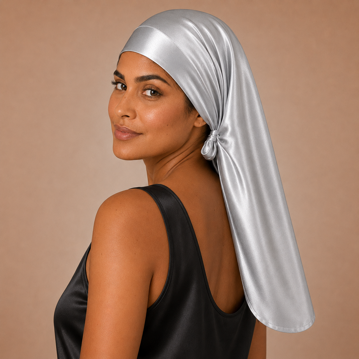 Woman in shiny silver reversible silk bonnet and black sleeveless top looks over her shoulder against a plain background.