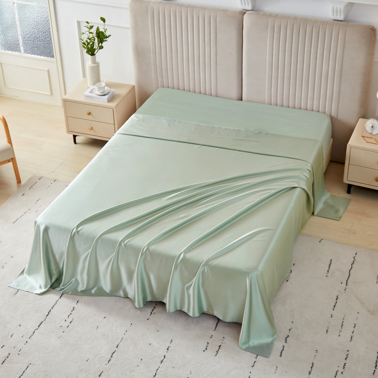 Sage silk flat sheet draped over a neatly made bed in a bright, modern bedroom