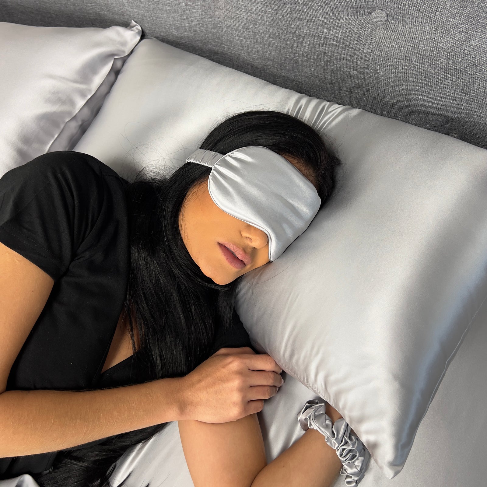 Woman sleeping on bed wearing silk sleep mask for eyes with matching pillows and sheet