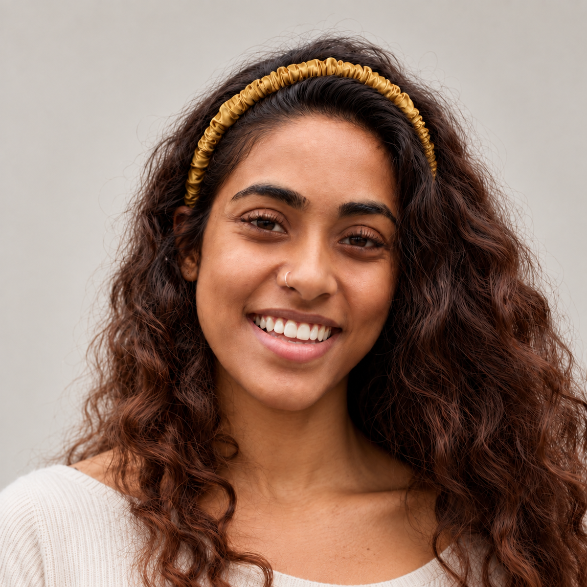 Woman with long curly hair and a yellow mulberry silk headband smiles at the camera against a plain background.