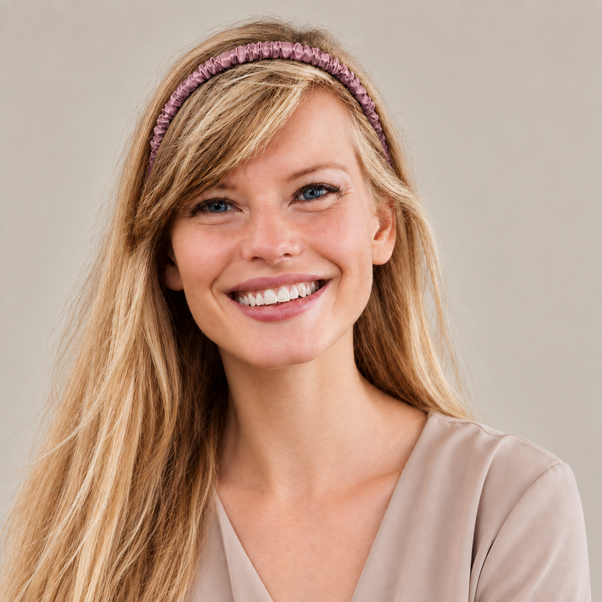 Woman with long blonde hair, in a mulberry silk headband and beige blouse, smiling at the camera against a plain background.