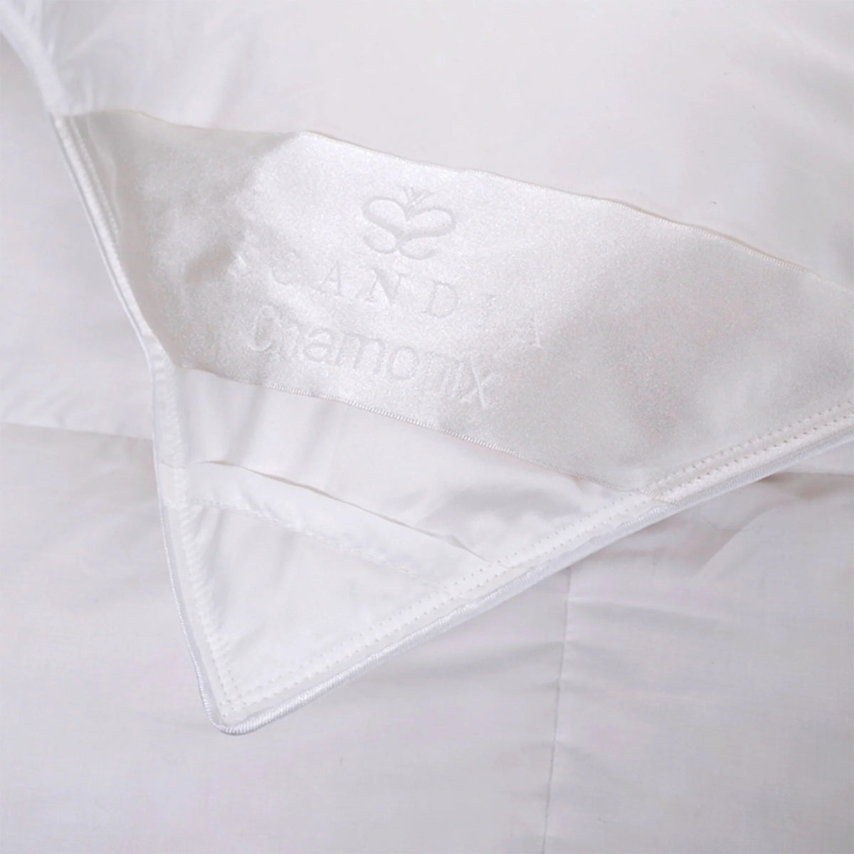 A close-up of a white luxury bedding comforter corner with a satin label that reads Scandia Chamonix.