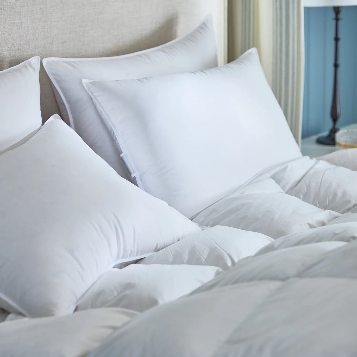 A neatly made bed with a luxury pillow, white comforter, and beige headboard in a softly lit bedroom.