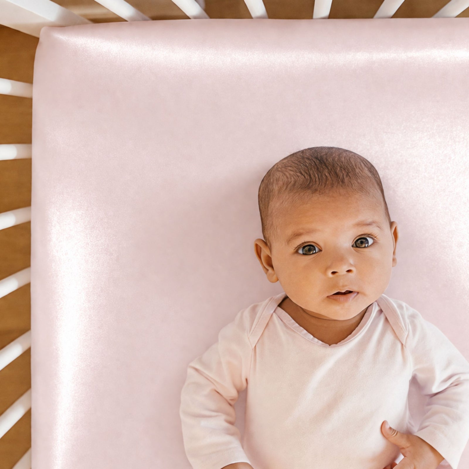 White toddler bed with a pink silk pillow, stuffed sloth, pink flower art on wall, and flower-patterned rug on floor.