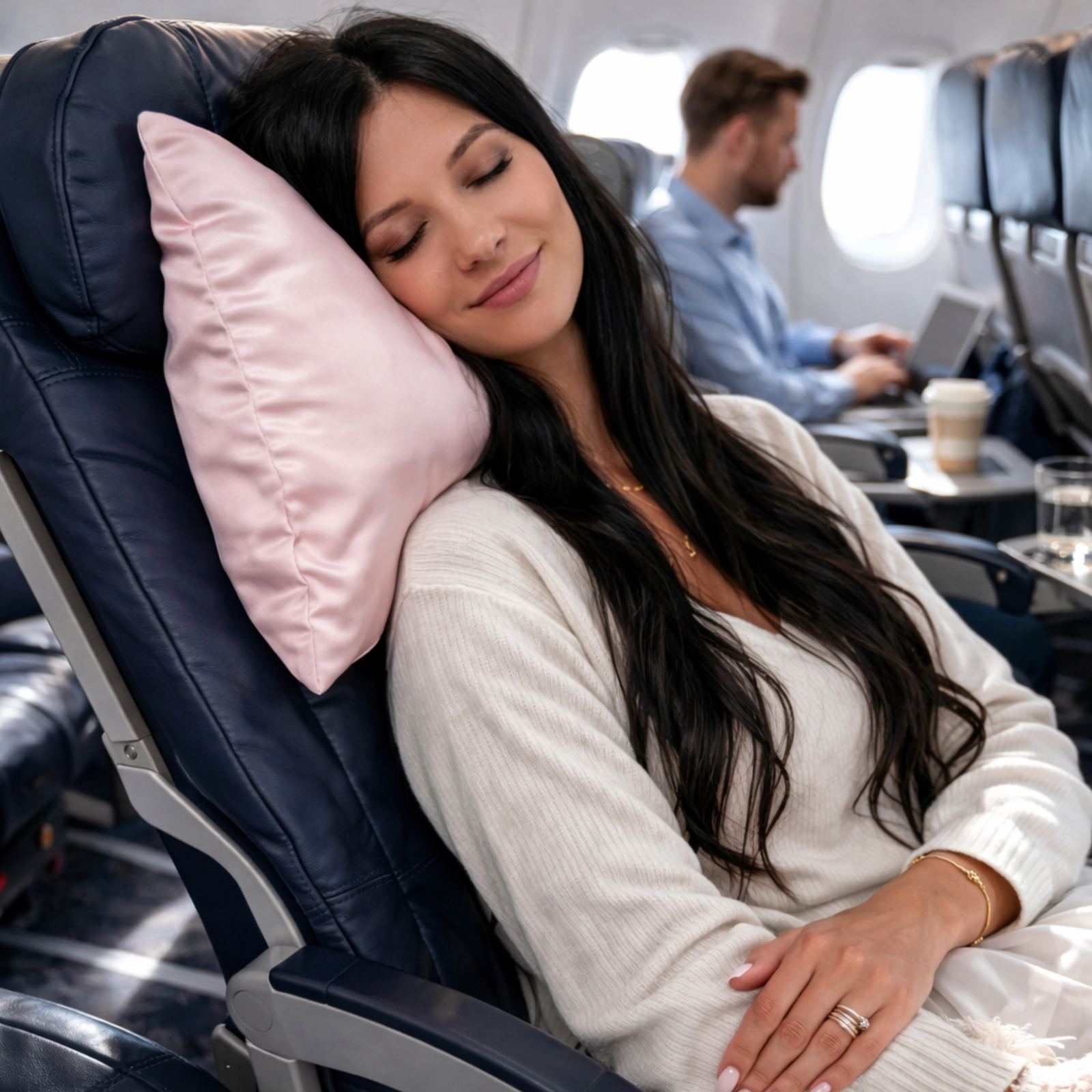 Woman sleeping on an airplane with a pink silk travel pillow, surrounded by airplane interior.
