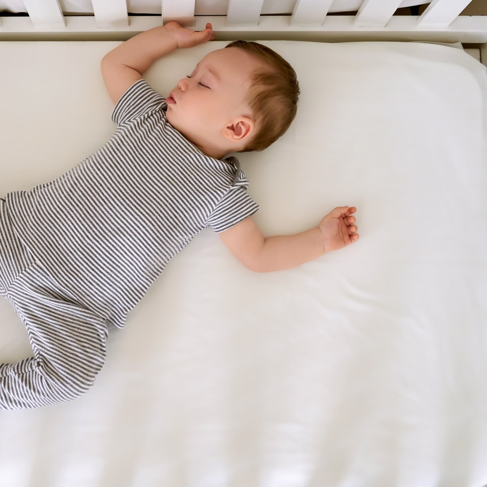 White toddler bed with a silk baby crib sheet, pillow, blue whale plush, under a whale painting on a wave-patterned rug.